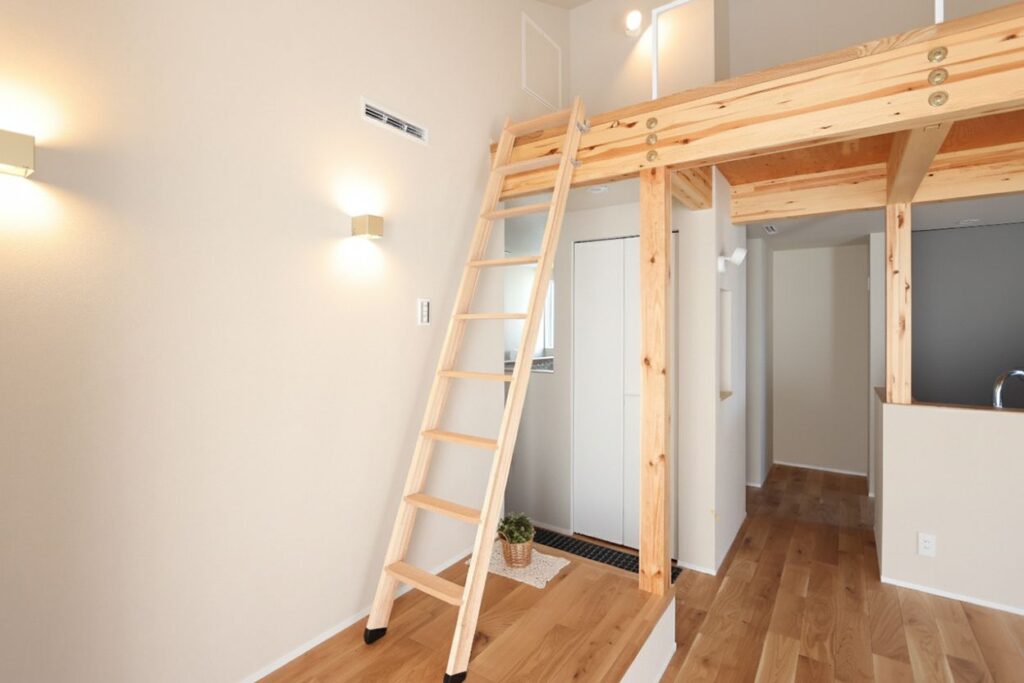 白い壁と木目が調和するナチュラルモダンな空間。小上がりからロフトへ続く木製のはしごが設置され、ブラケットライトの温かい光が立体的な間取りを優しく照らしています