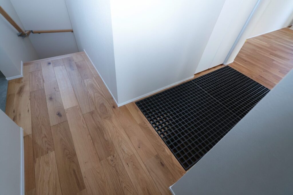 階段上のホールに設けられた、無垢材のフローリングと黒いグレーチング（格子状）の床。白い壁と木の温もりに黒のアクセントが効いた、階下へ光と風を届けるナチュラルモダンな間取りです。