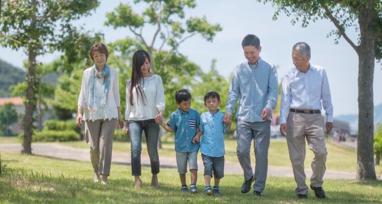 写真：手を繋いで公園を歩く三世代家族